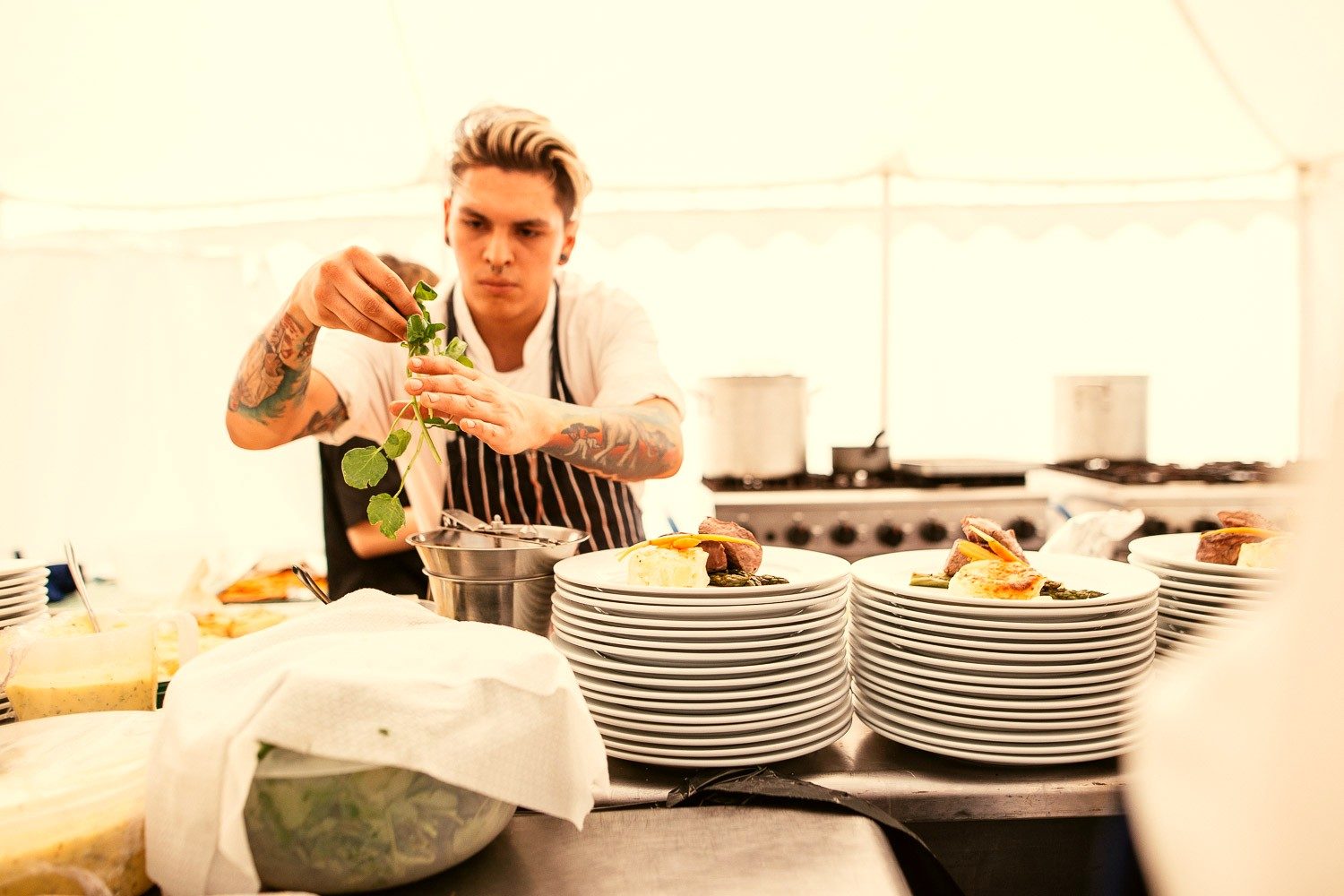 A chef finishing plated fillet dishes with fresh watercress in the marquee kitchen.