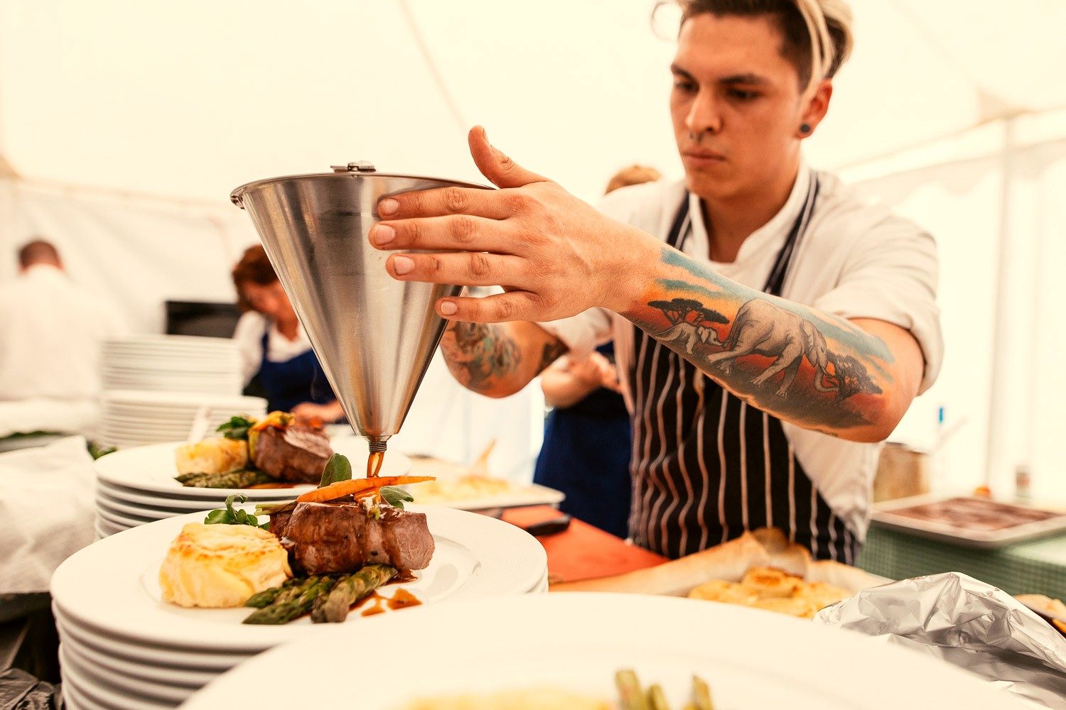 A chef finishing a plated dish with sauce from a jug.
