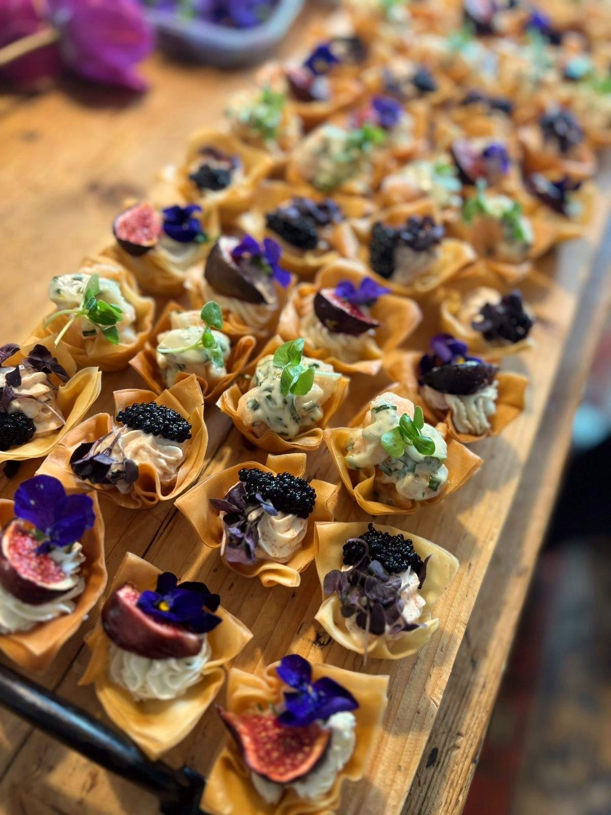 A close-up of filo canapes topped with fig, caviar and edible flowers.