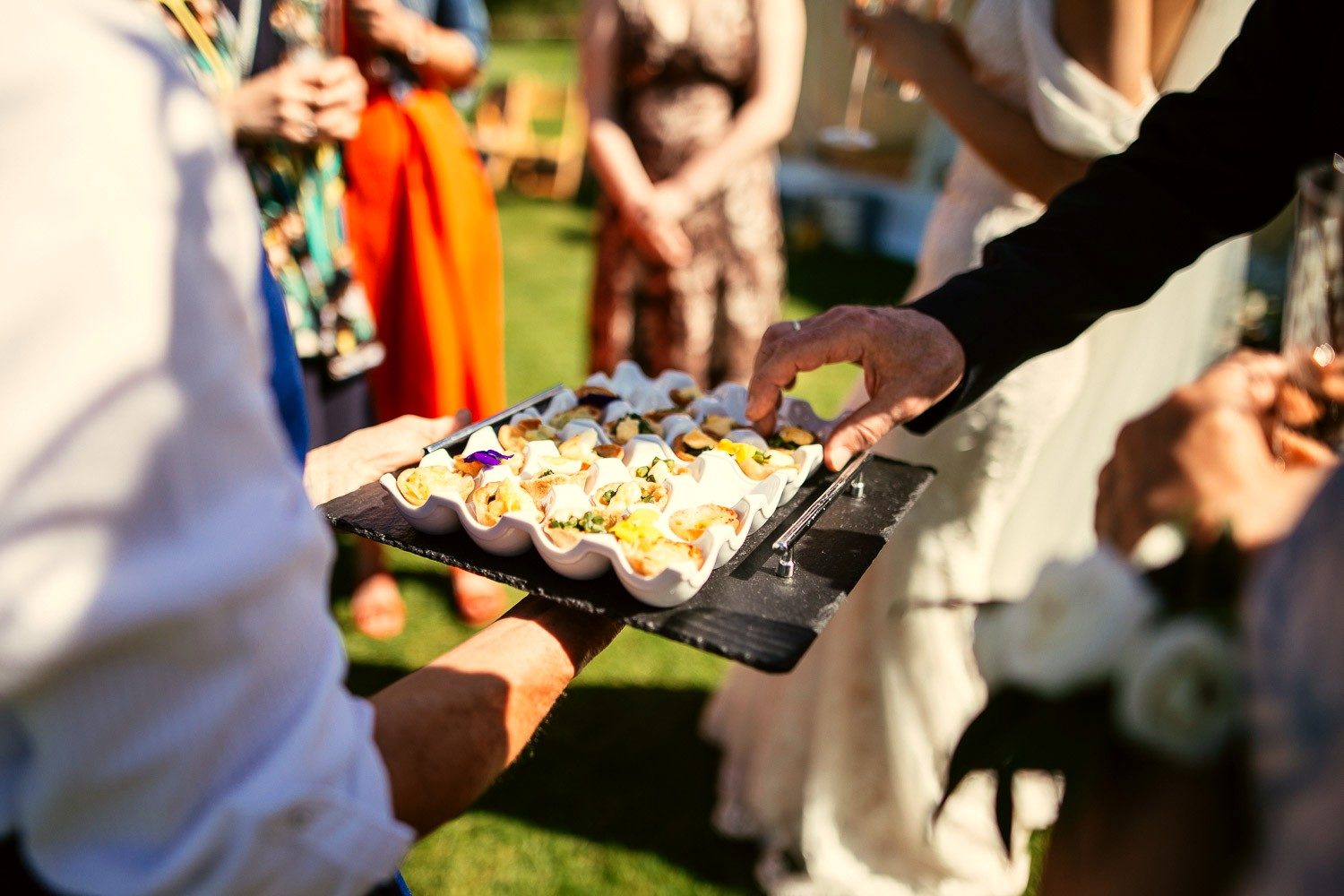 Wedding guests reaching for a tray of canapes in the garden.