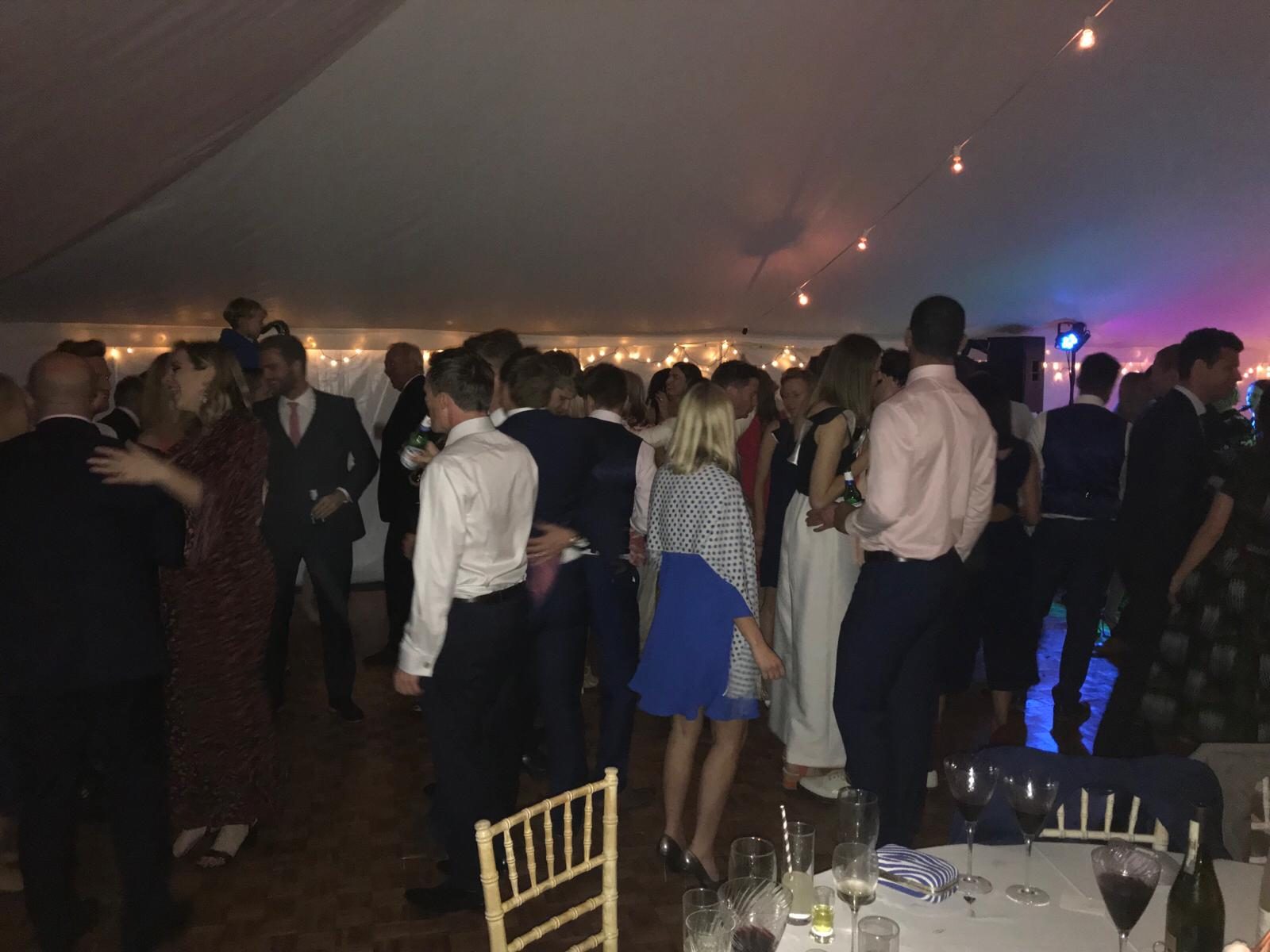 Guests dancing together in a marquee lit with fairy lights.
