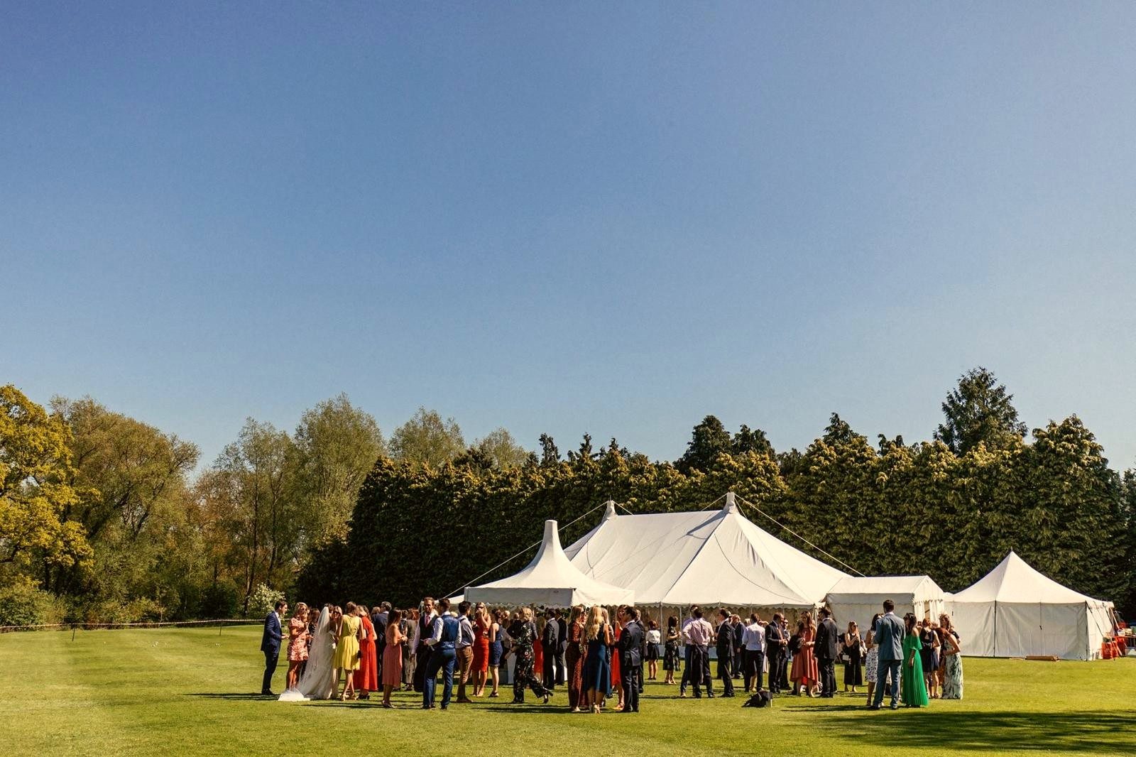 A marquee reception on the lawn with guests gathering in the sunshine.