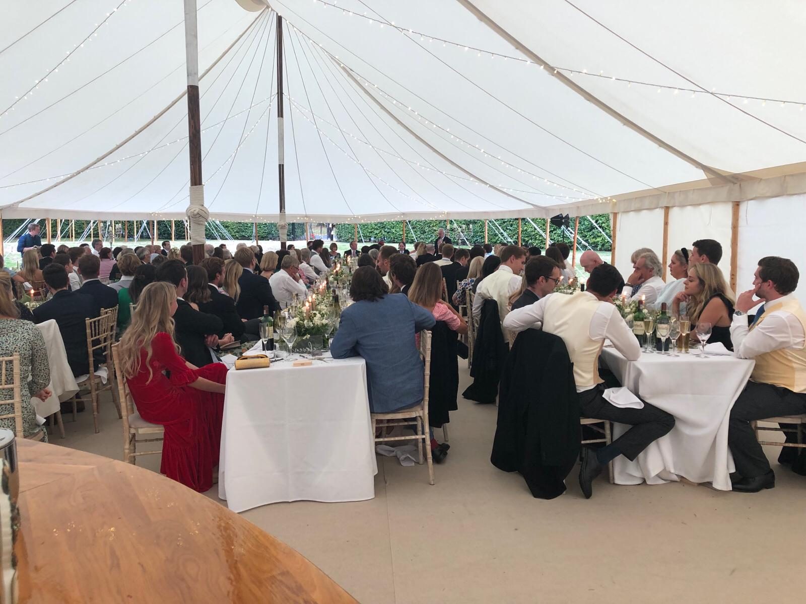 Guests seated for speeches at a marquee wedding reception.