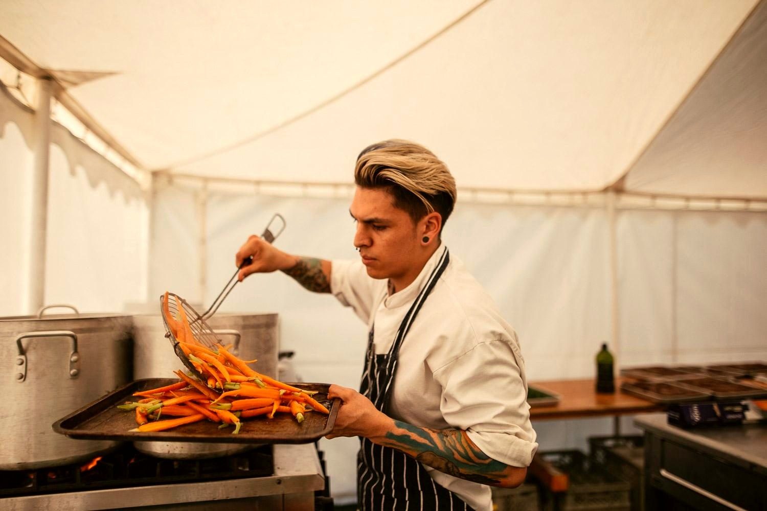 A chef preparing trays of freshly cooked carrots in the marquee kitchen.