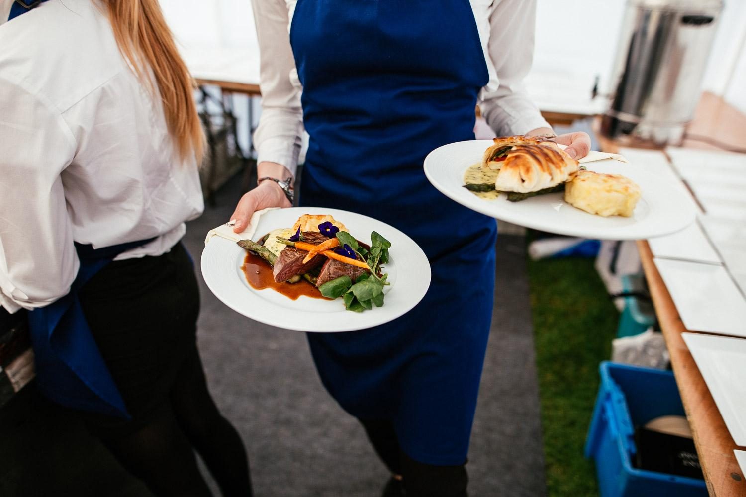 A member of staff carrying two plated courses at a marquee event.