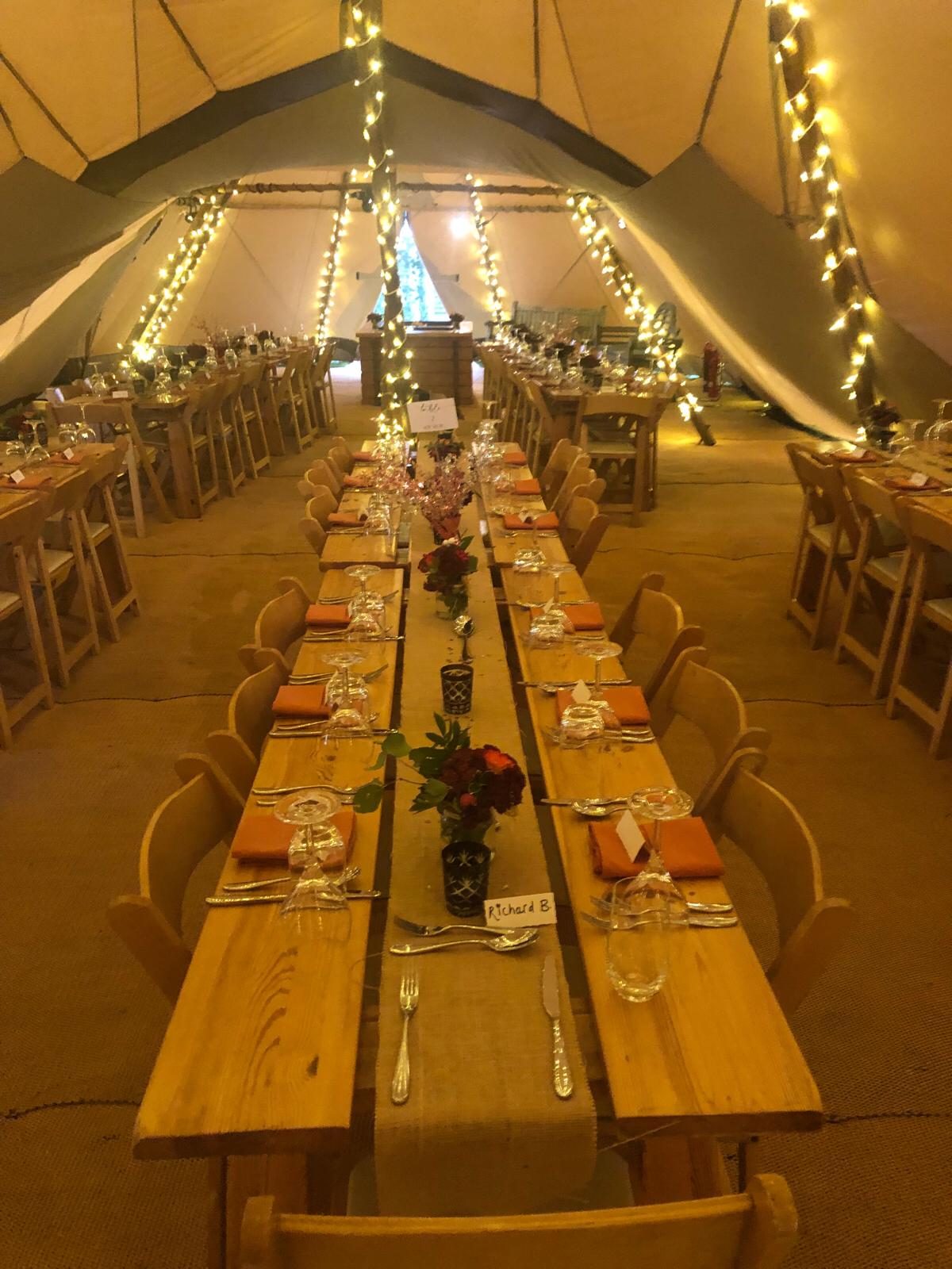 A tipi laid with long tables, fairy lights and warm evening lighting for a wedding.