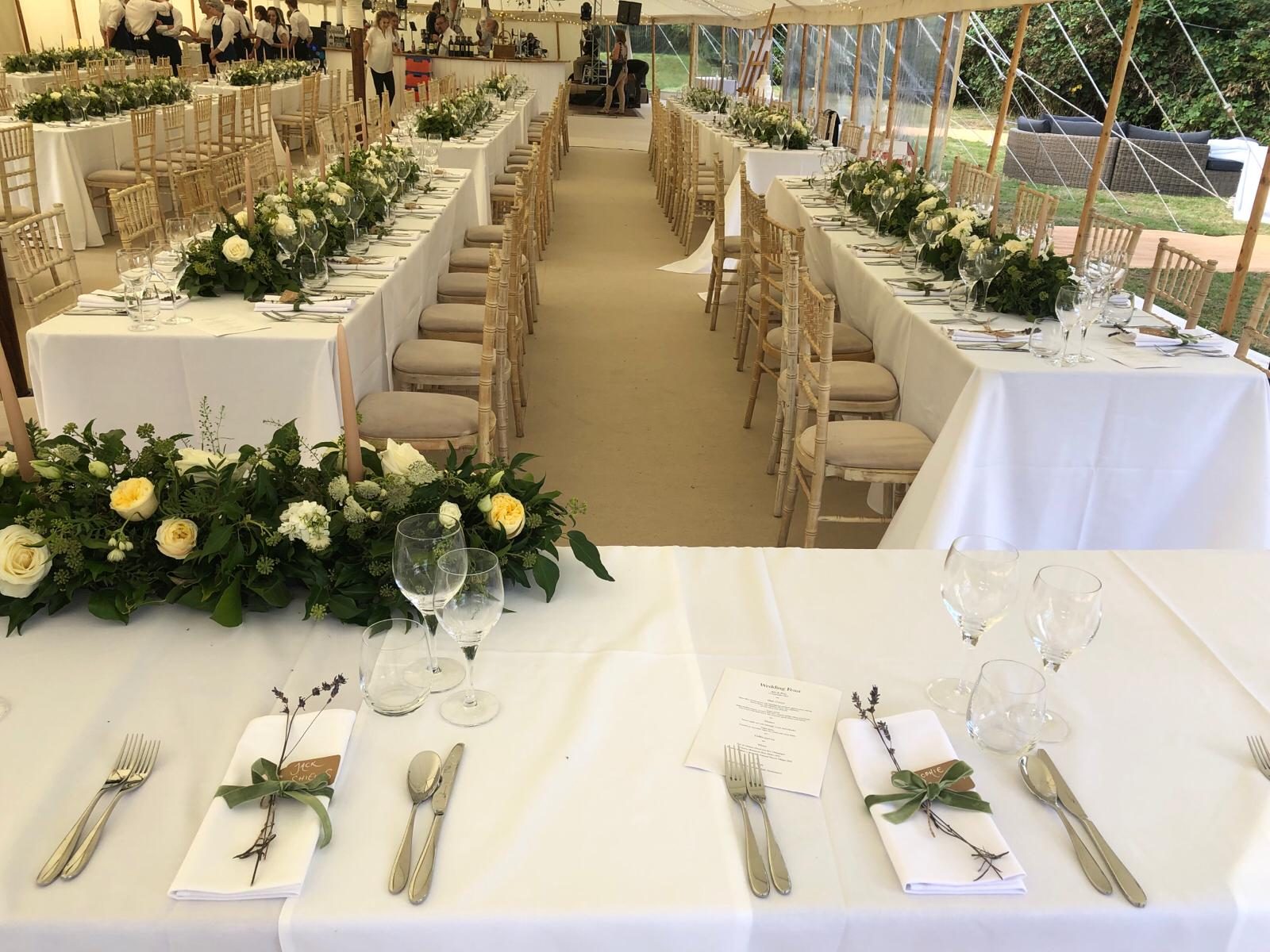 A sailcloth marquee laid for a wedding breakfast, dressed with white linen and seasonal flowers.